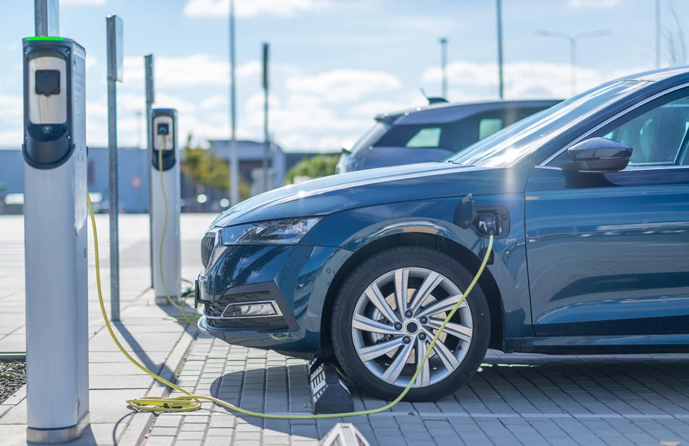 Blue electric vehicle charging at public charging station on paved lot.
