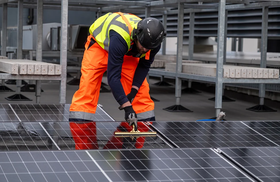 Construction worker in safety gear installing solar panels on a rooftop.