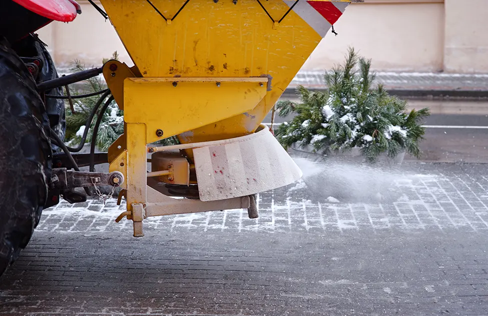 Yellow snow plow truck spraying salt and de-icer on a snowy street during winter weather.